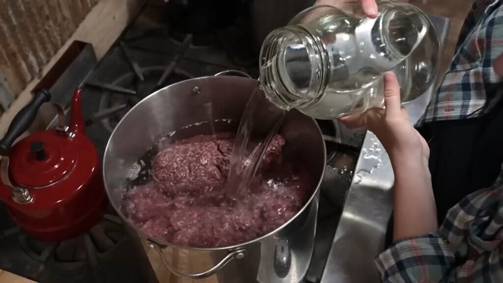 A woman adding water to a pot of ground beef.