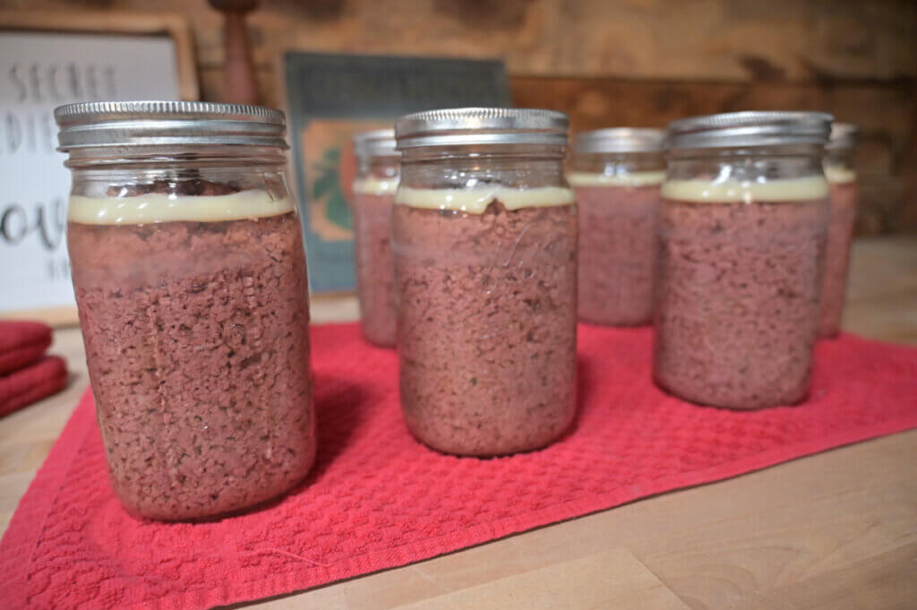 Finished jars of canned ground beef cooled on the counter.