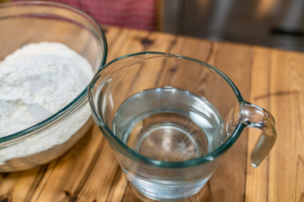 A bowl of flour and measuring cup of water.