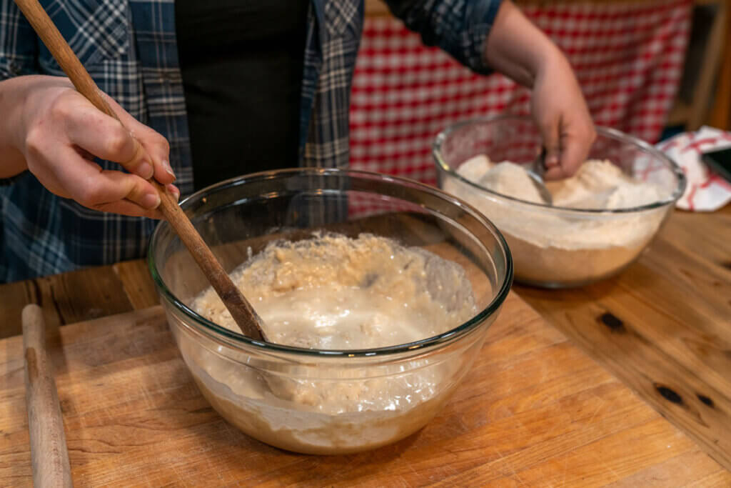 A woman adding flour to a bowl of dough.