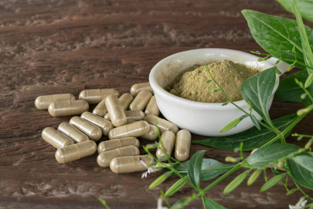 Herb capsules on a table with a bowl of dried herbs.