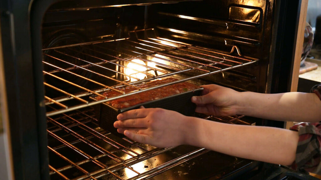 Hands sliding a pan of meatloaf into the oven.