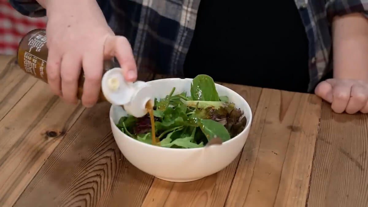 Adding vinaigrette salad dressing onto a bowl of fresh greens.