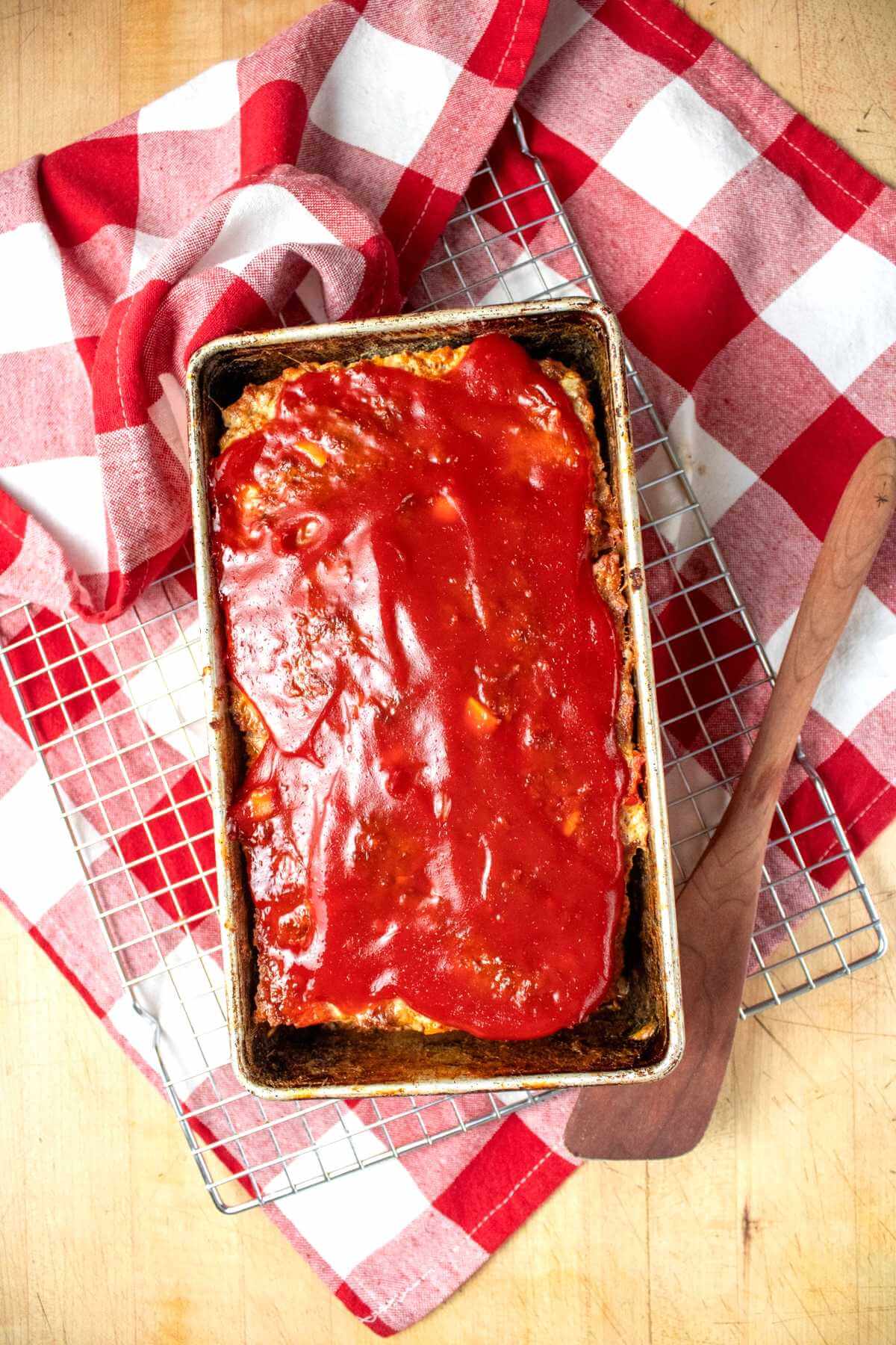Finished glazed meatloaf in its loaf pan on a wire rack.