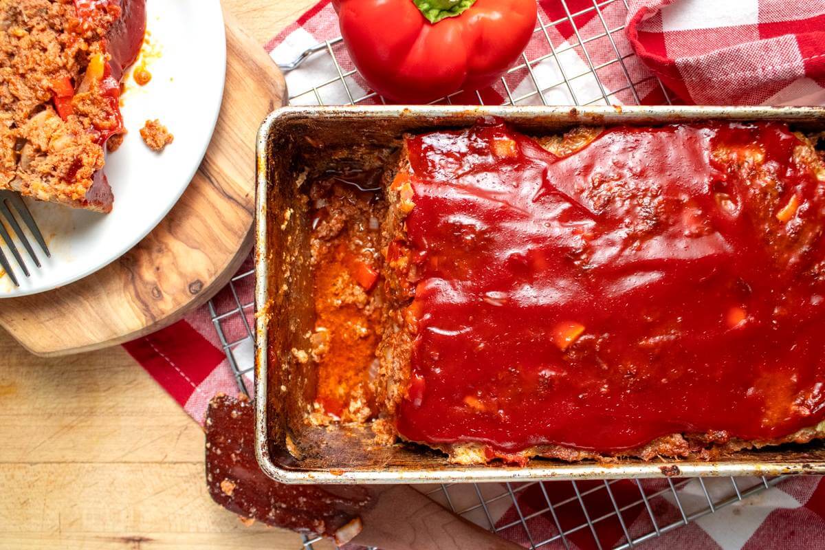 Glazed freezer meatloaf in a loaf pan with a slice served on a plate.