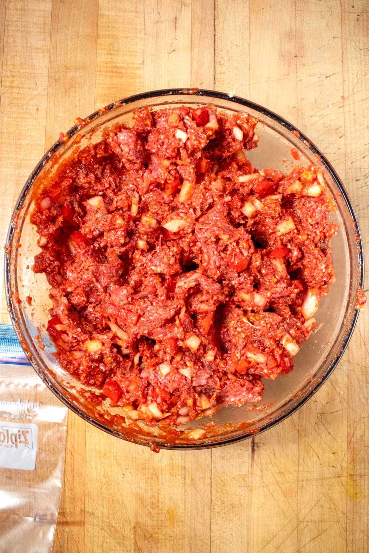 Mixed raw meatloaf with chopped peppers and onions in a glass bowl.