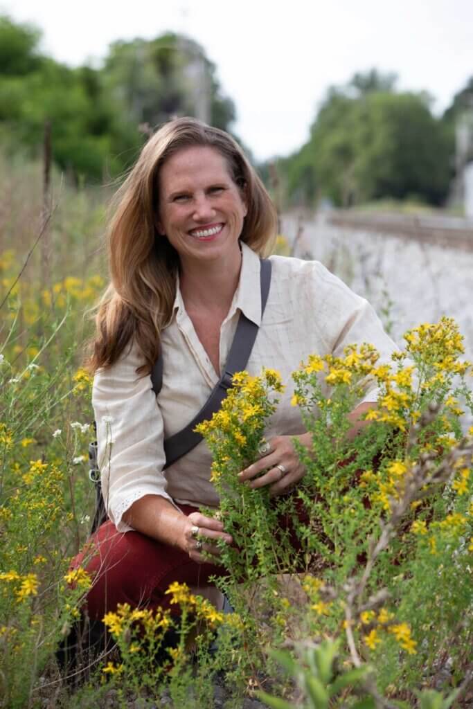 A woman crouched in a field with foraged plants.