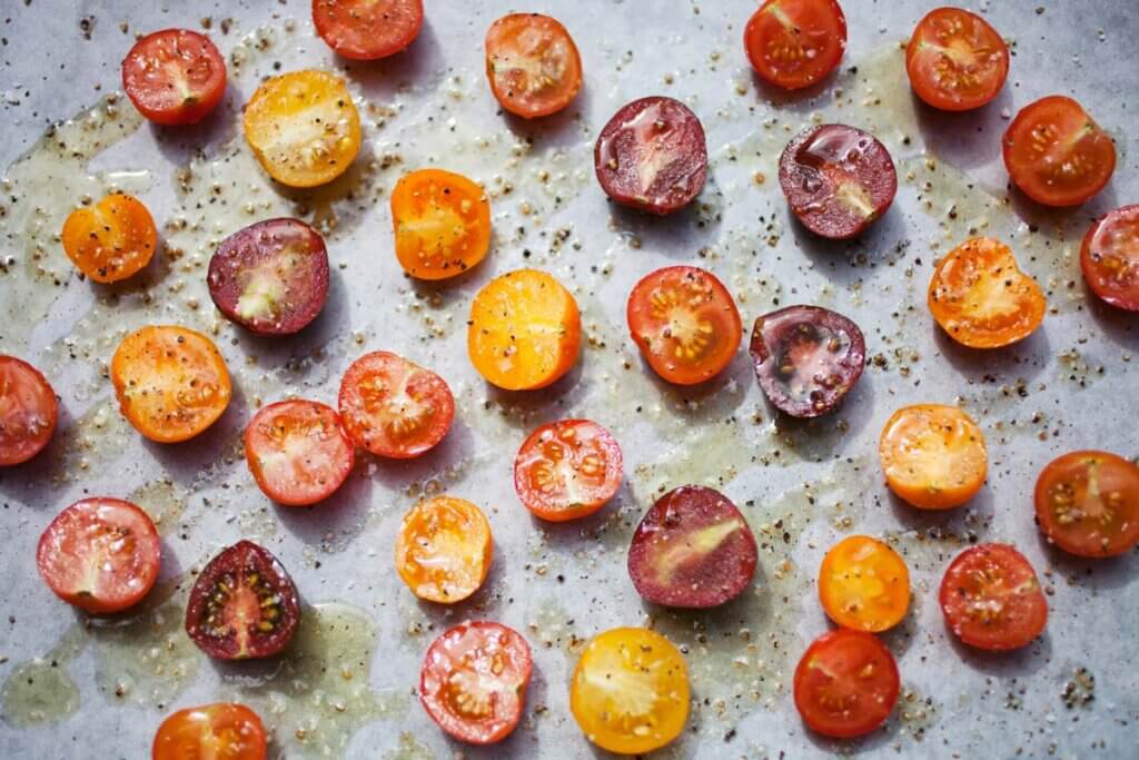 Sliced tomatoes on a tray sprinkled with herbs.