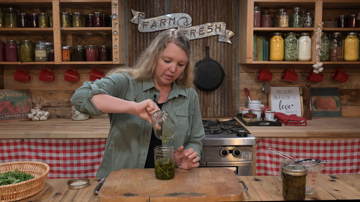 A woman pouring oil into a jar of medicinal herbs.