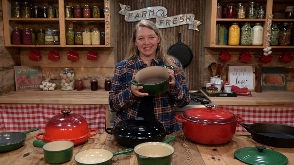 A woman holding up an enameled cast iron pot in the kitchen.