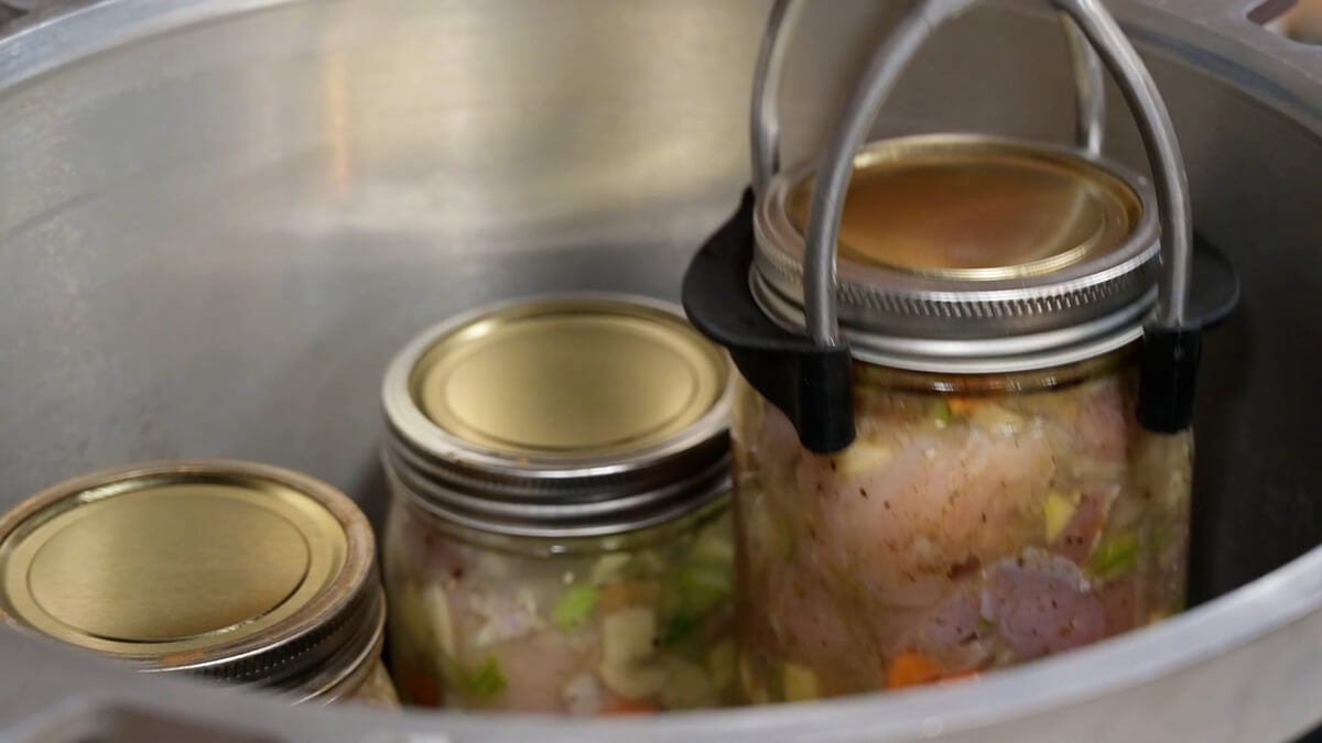 Jars of chicken and gravy going into a pressure canner.