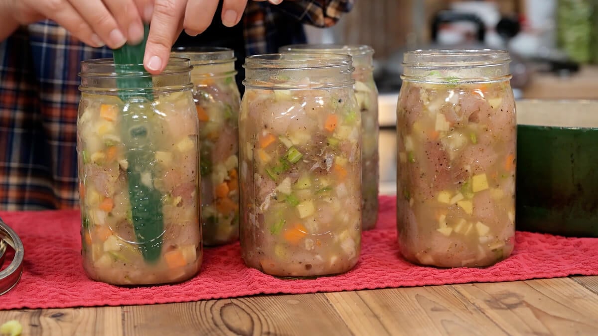 A woman using a bubble popper in jars of chicken and gravy.