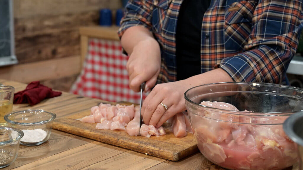 A woman chopping chicken breasts on a cutting board.