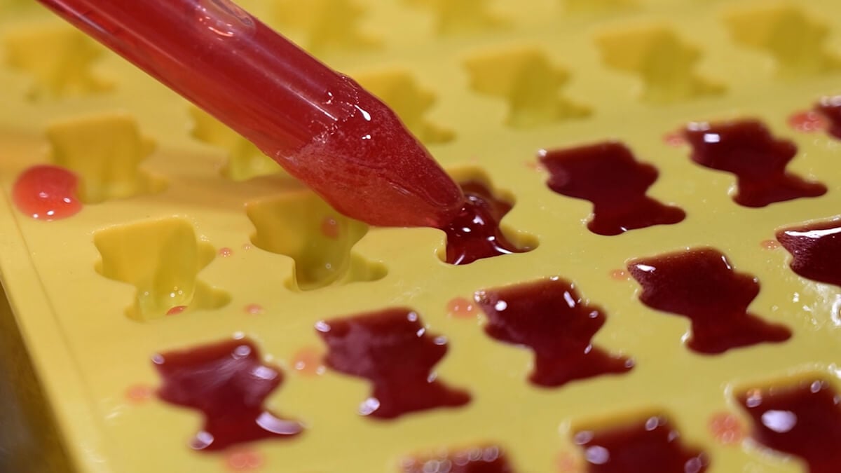 Elderberry syrup mixture being poured into silicone gummy bear molds with a dropper.