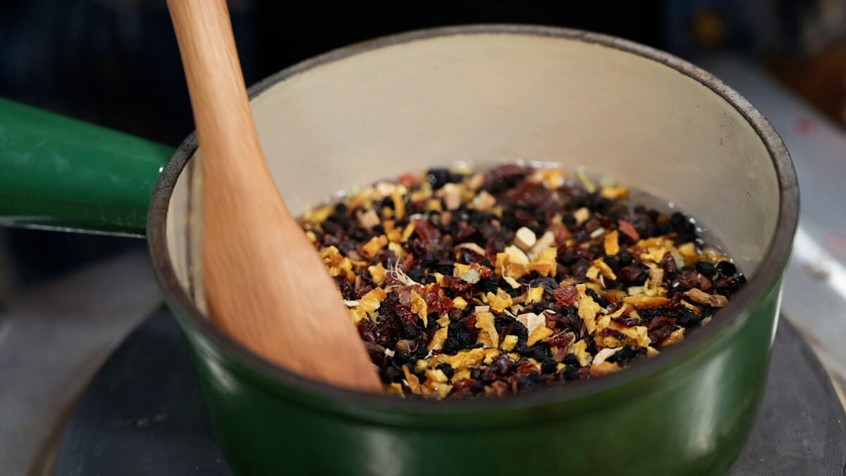 Elderberry syrup mix in a pot with a wooden spoon.