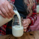 A woman pouring a glass of raw milk into a Mason jar.