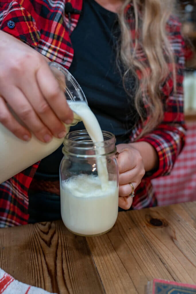 A woman pouring a glass of raw milk into a Mason jar.