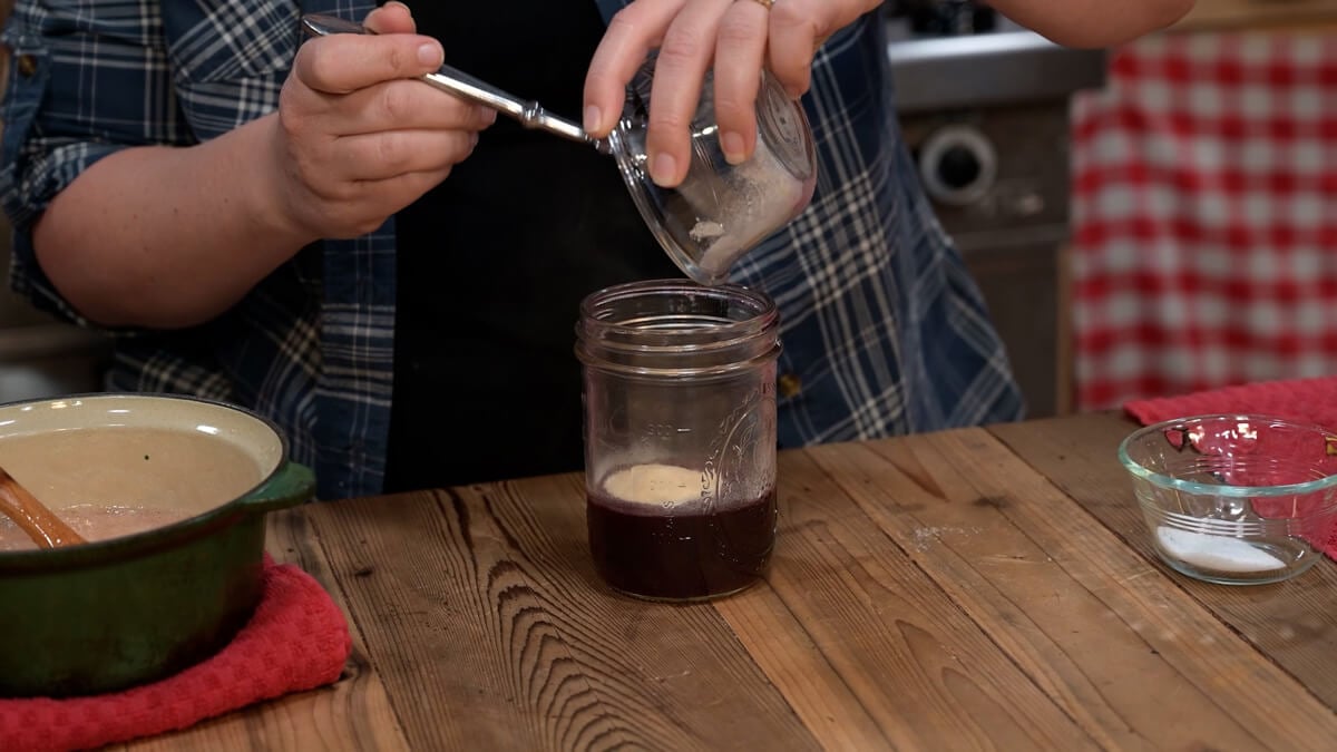 Gelatin powder being poured into a glass of elderberry tea concentrate.