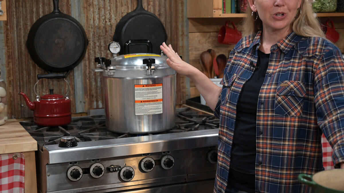 A woman standing next to a pressure canner in the kitchen.