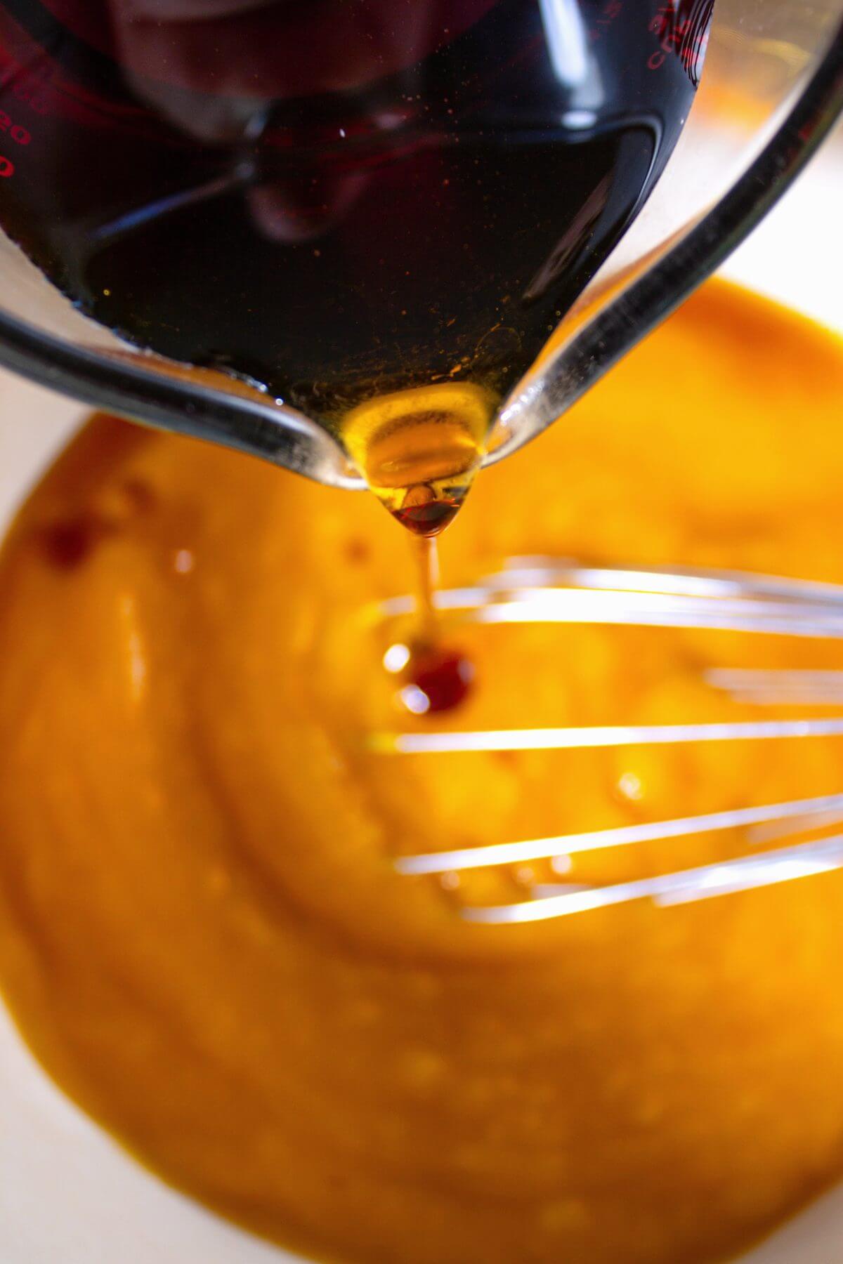 Maple syrup pouring into pumpkin pur&eacute;e beside a wire whisk.