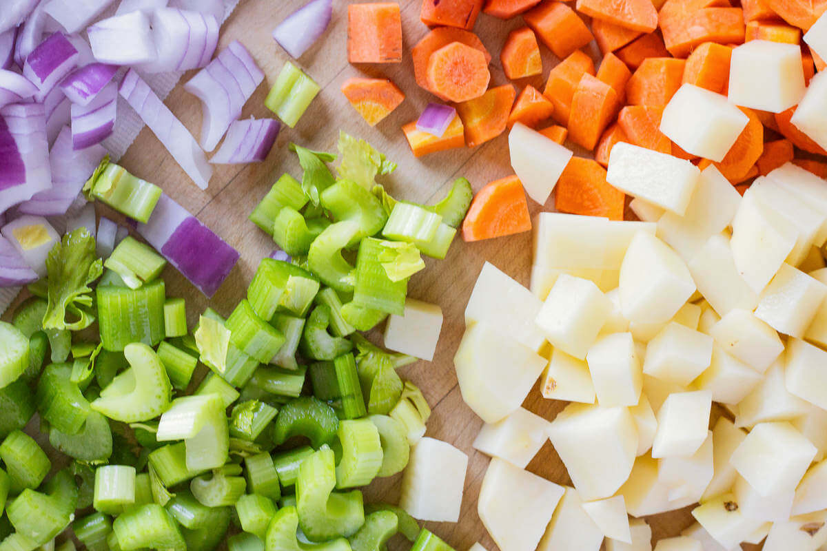 Chopped onions, celery, carrots and potatoes on a cutting board.