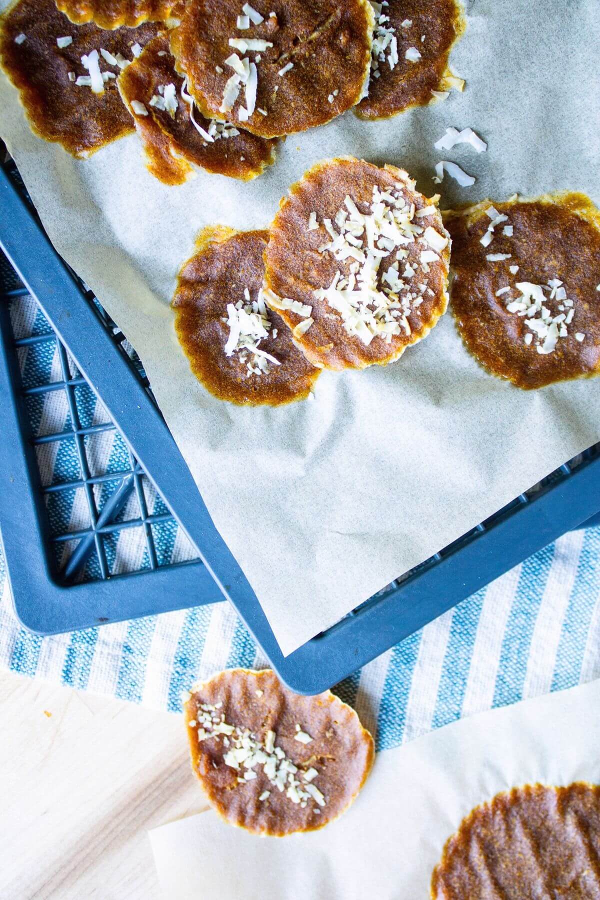 Dried pumpkin leather rounds with coconut on parchment beside a blue tray.
