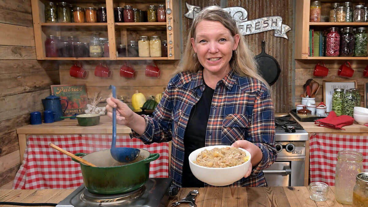 Carolyn holding a bowl of chicken and gravy beside a pot in the kitchen.