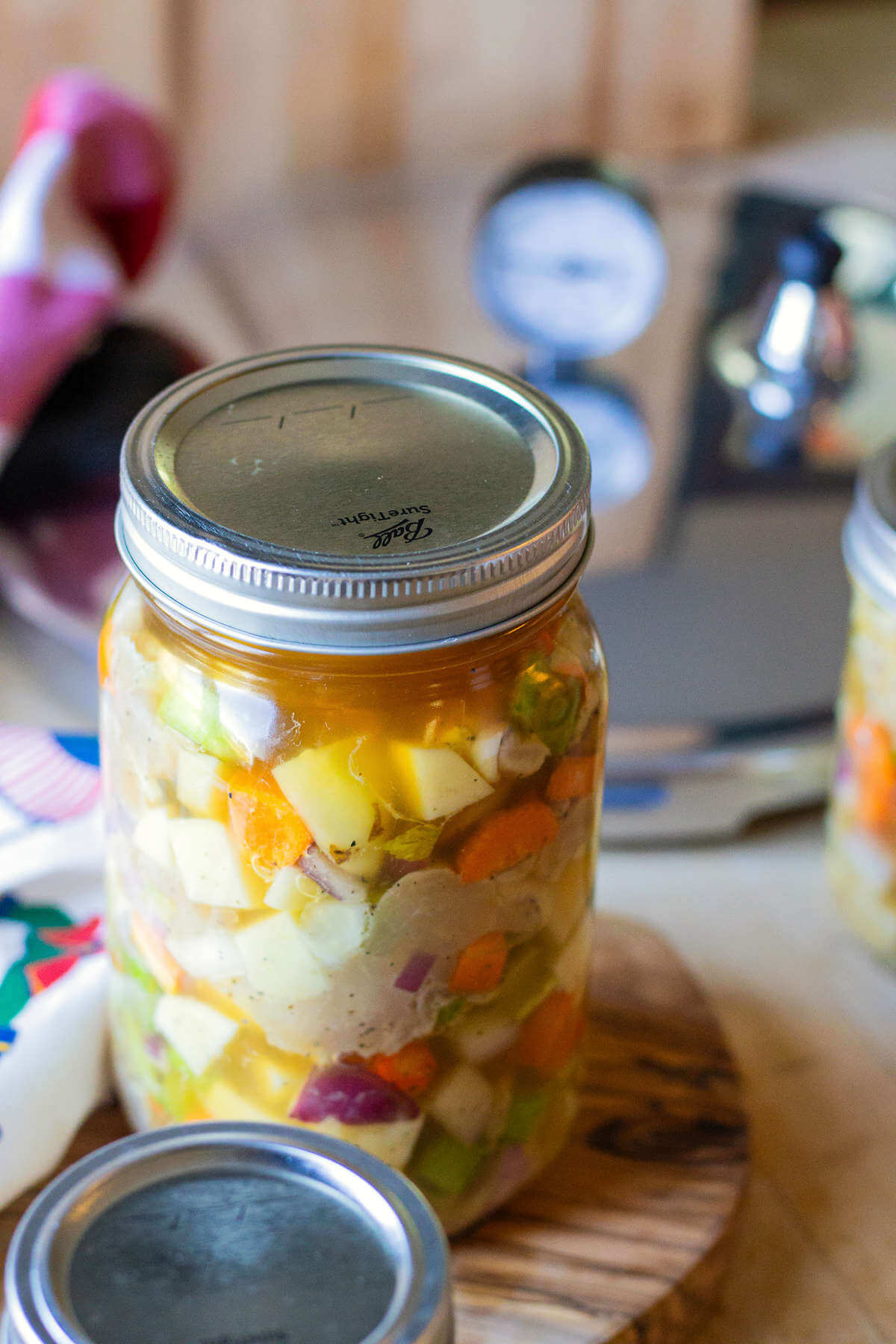 Tall lidded jar of chicken and vegetables on a wooden board.