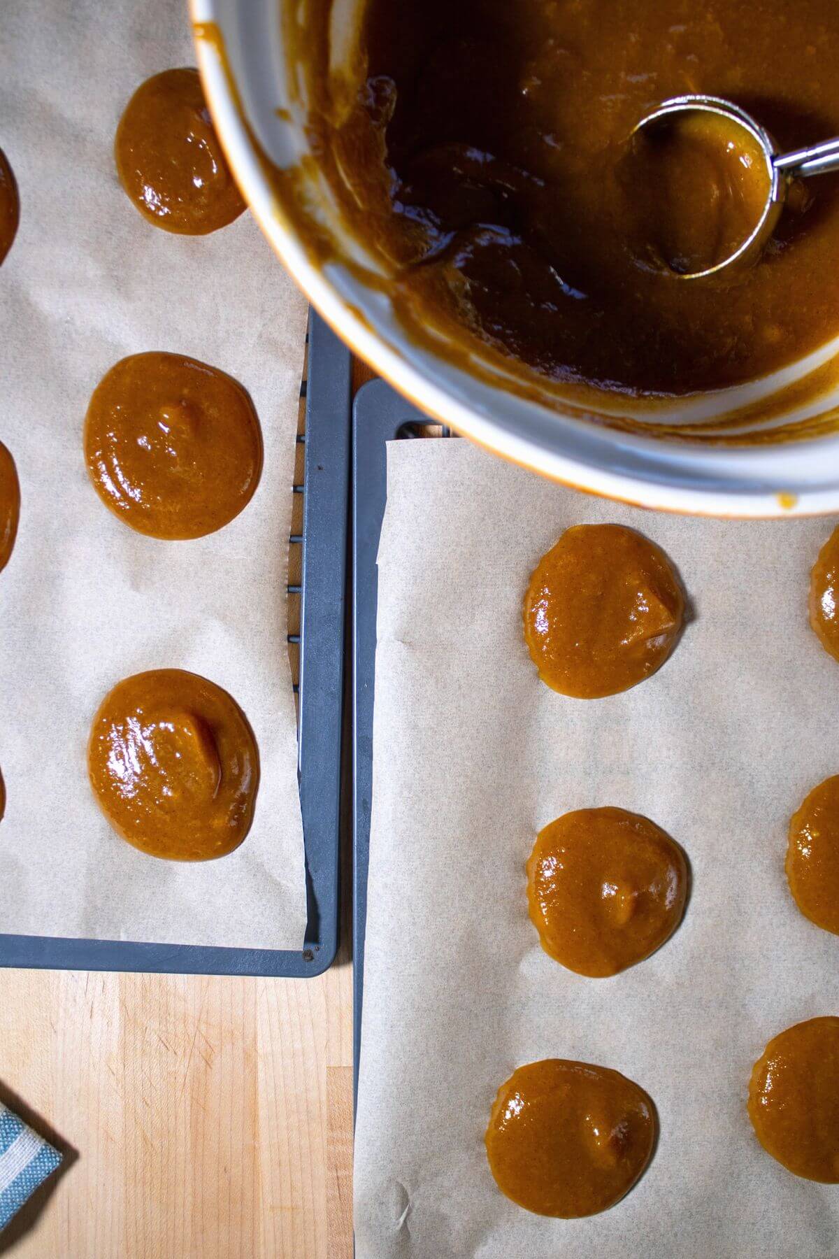 Rounds of pumpkin mixture on parchment-lined trays beside a mixing bowl and spoon.