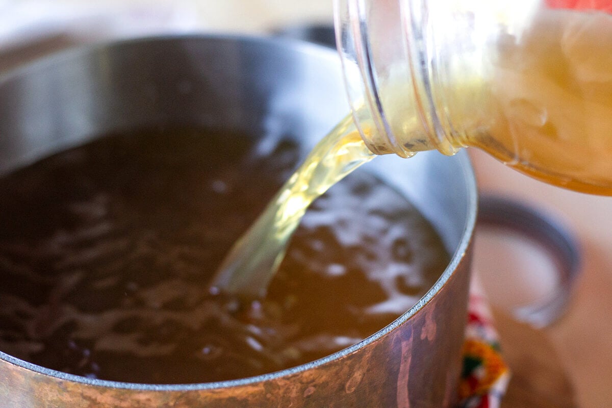 Chicken broth being poured from a glass jar into a pot.