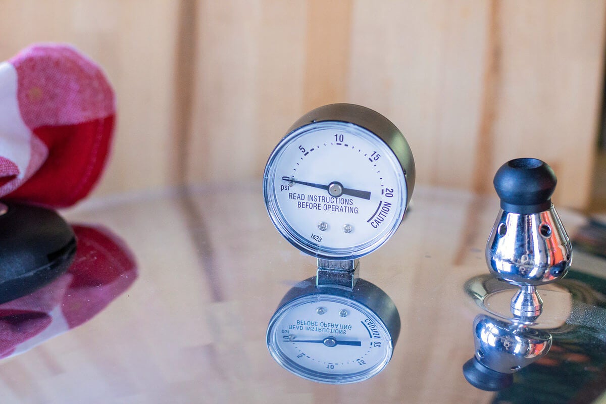 Pressure canner dial gauge and metal weight on a reflective lid.
