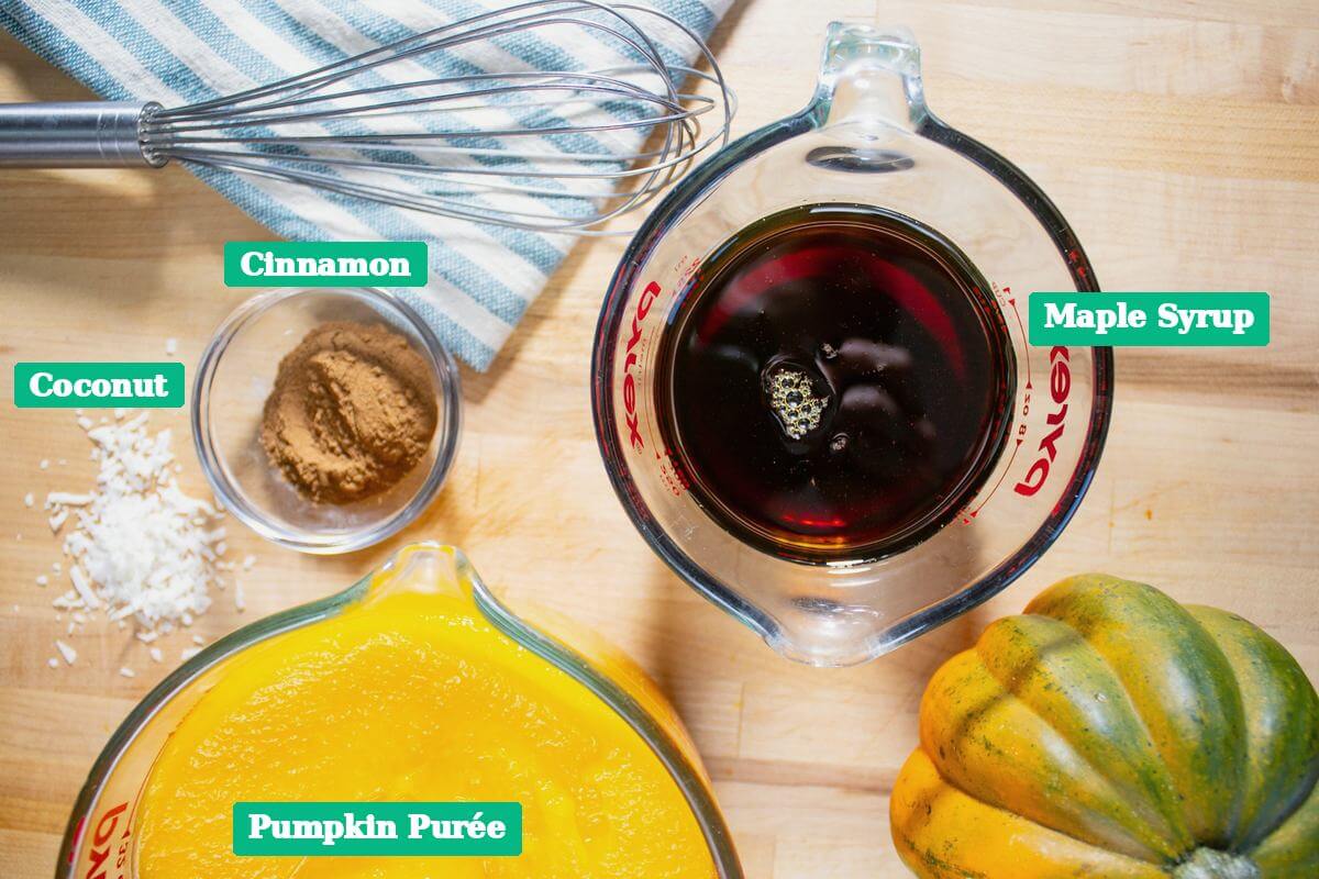 Coconut, cinnamon, maple syrup and pumpkin pur&eacute;e arranged on a wooden counter.