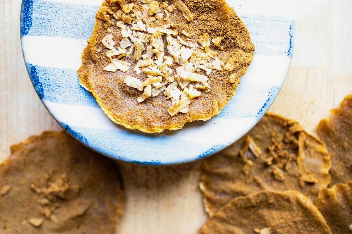 Coconut-topped pumpkin leather on a blue-striped plate with more rounds on the counter.