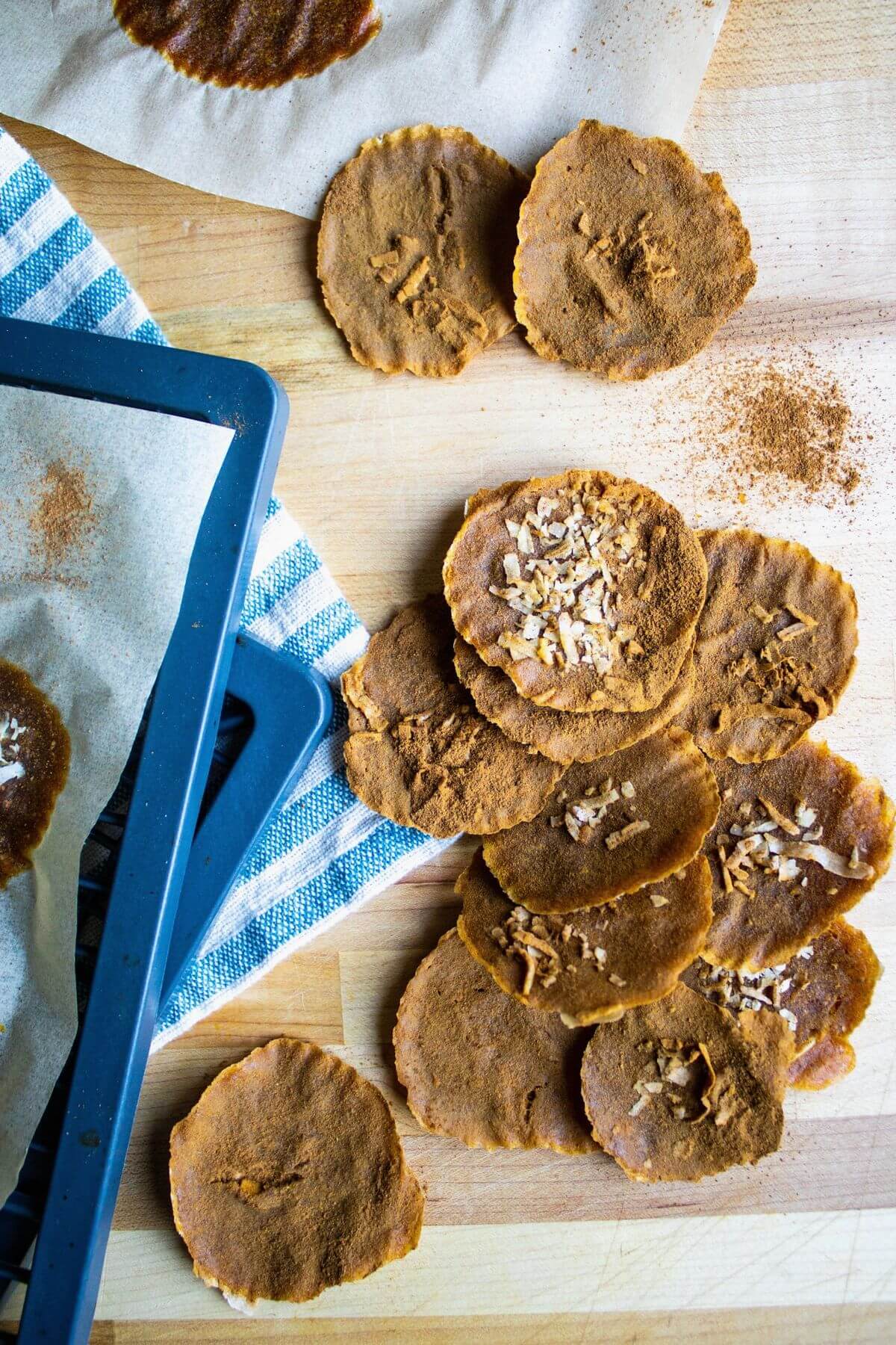 Pumpkin leather rounds arranged on parchment with scattered coconut and a blue tray.