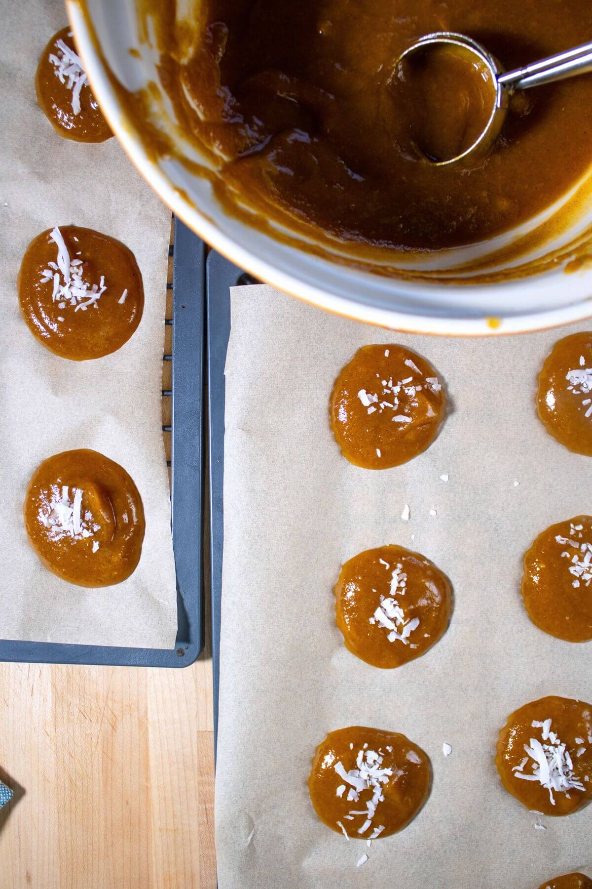 Pumpkin mixture portioned onto parchment-lined trays, with coconut sprinkled on several rounds.