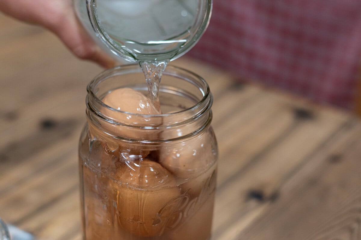 Lime water being poured over eggs in a glass Mason jar.