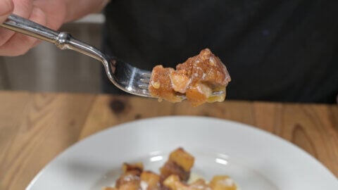 A bite of Apple Brown Betty on a fork with more served up on a white plate.