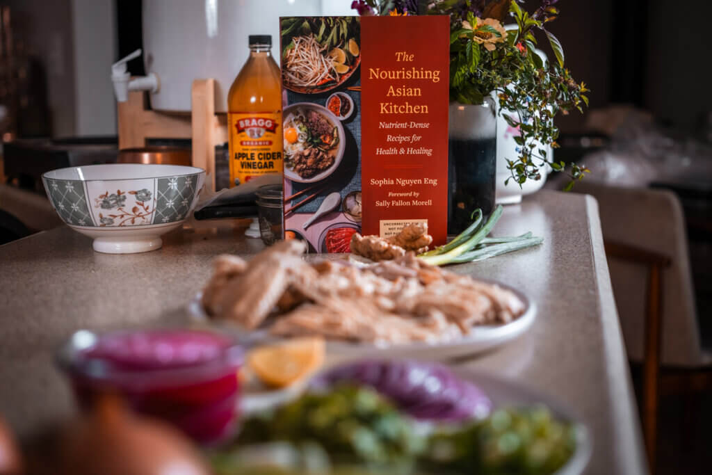 The Nourishing Asian Kitchen cookbook on a counter with recipes.