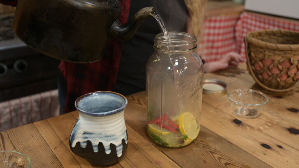 Water being poured into a half gallon Mason jar for herbal cold and flu tea.