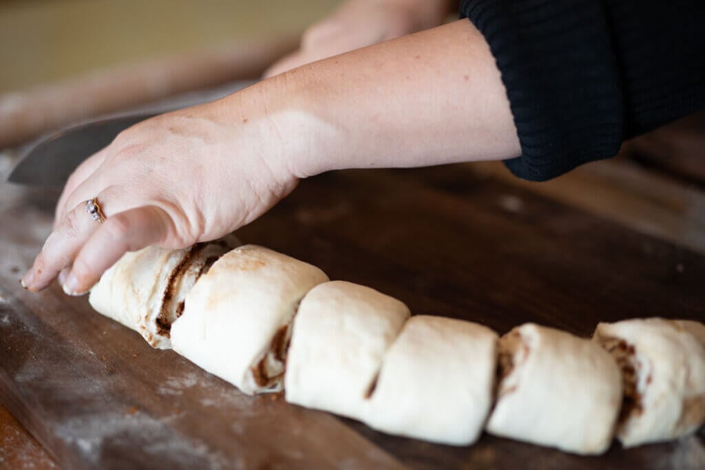 Hands slicing gluten free cinnamon roll dough.