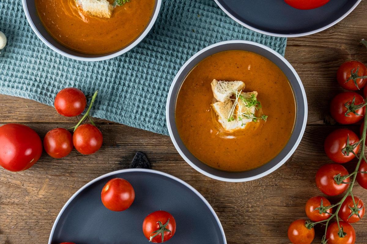 Tomato soup topped with bread cubes and herbs in a bowl.
