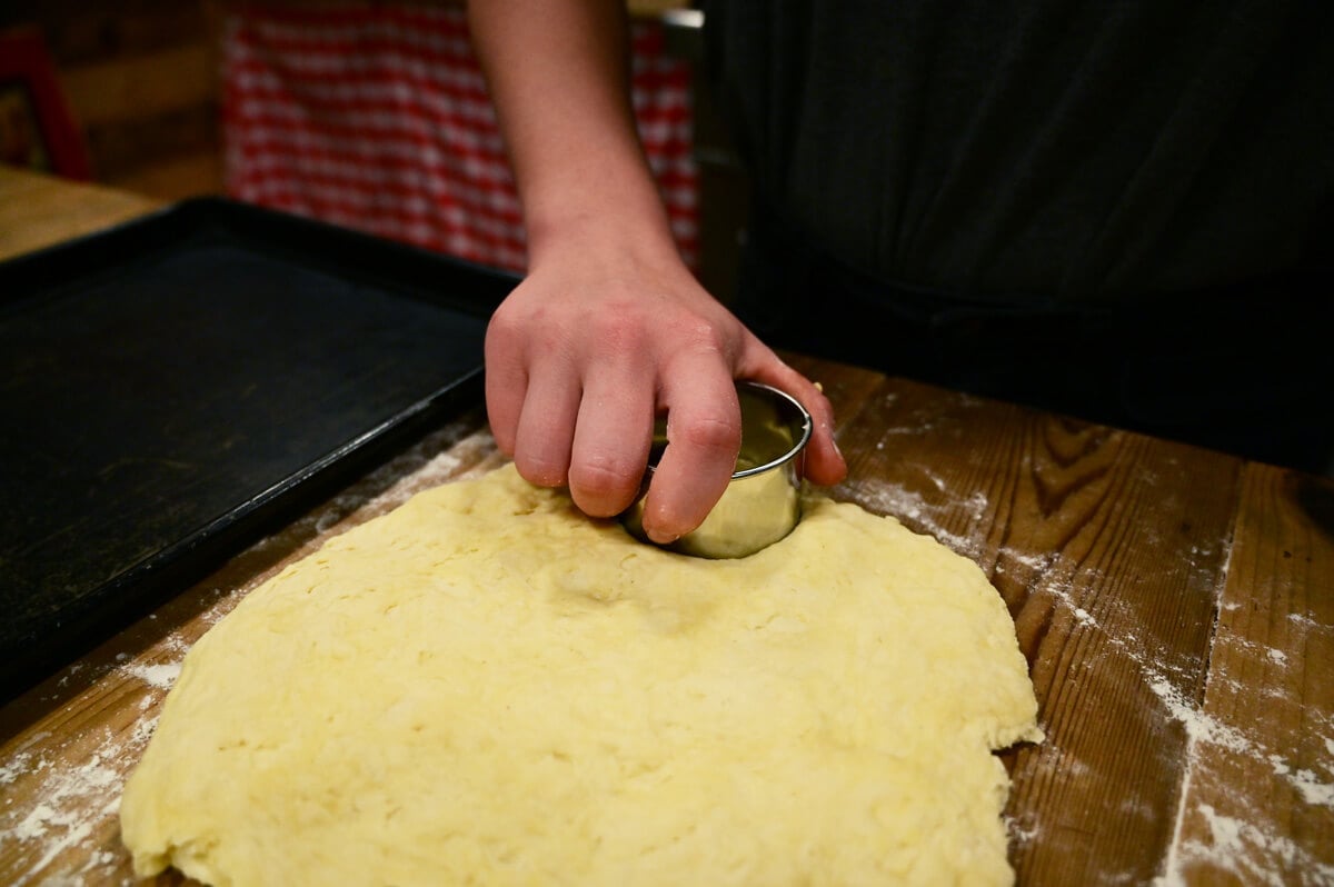 A hand with a biscuit cutter cutting out biscuits.
