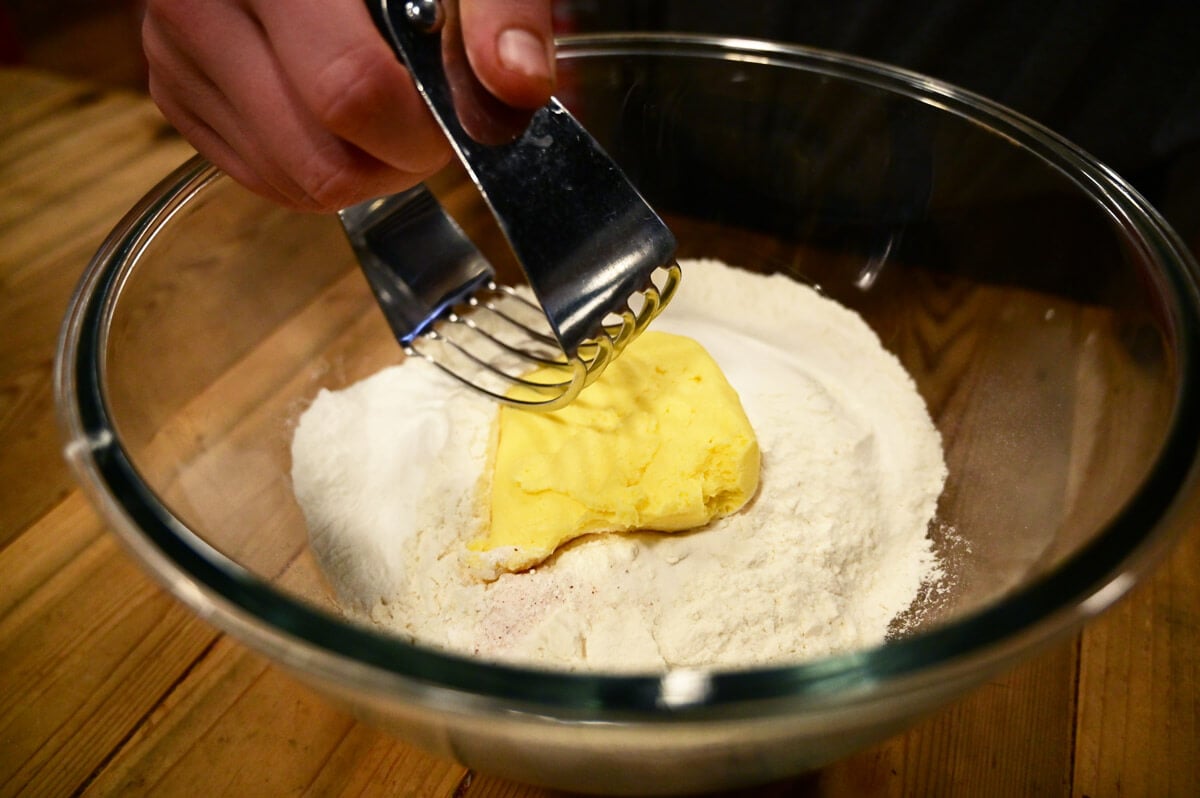 A pastry cutter cutting in butter into biscuit dough dry ingredients.