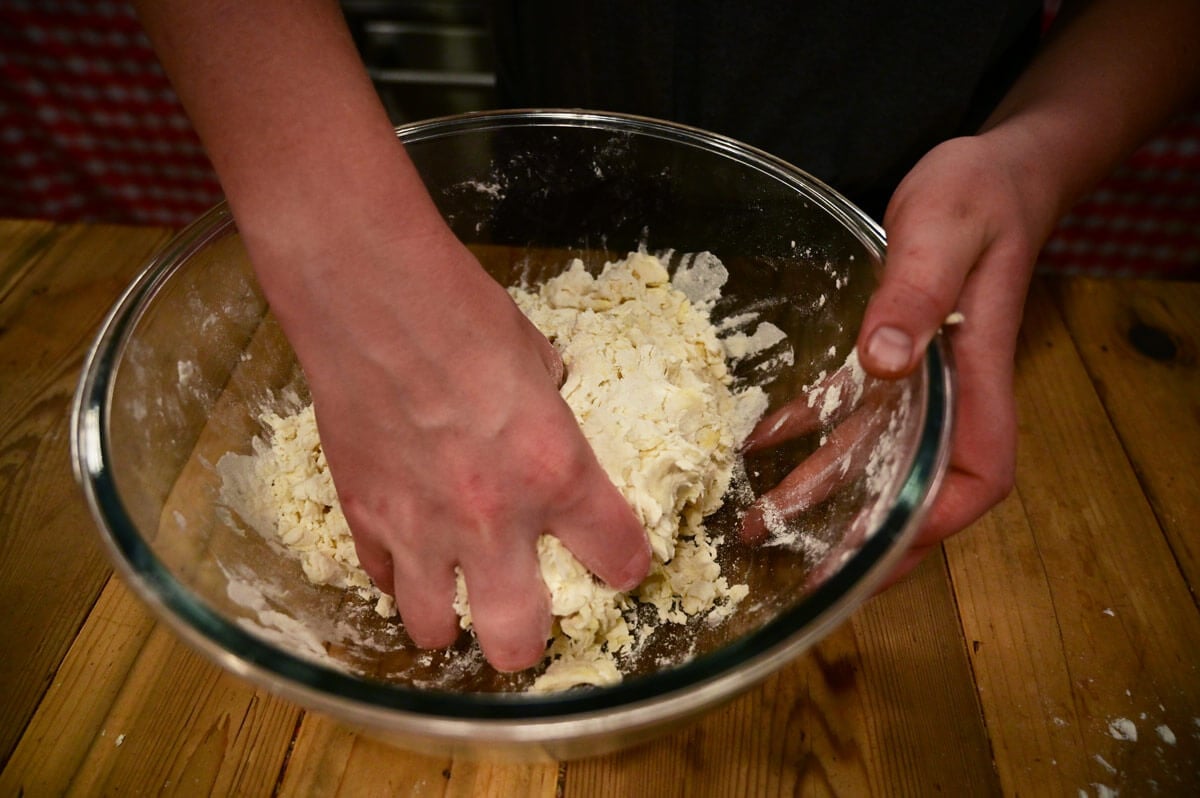 A girl's hand mixing biscuit dough in a glass bowl.