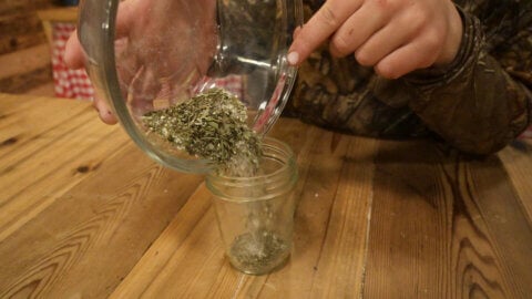 Garlic and herb seasoning being poured into a small Mason jar.