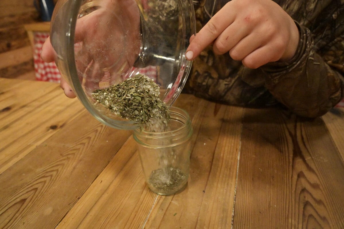 Garlic and herb seasoning being poured into a small Mason jar.