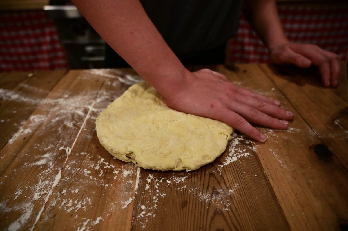 Biscuit dough being pressed out onto a wooden counter.