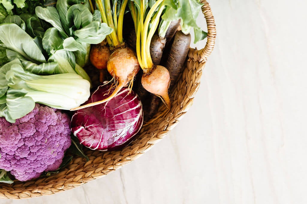 A basket of garden vegetables on a wooden counter.