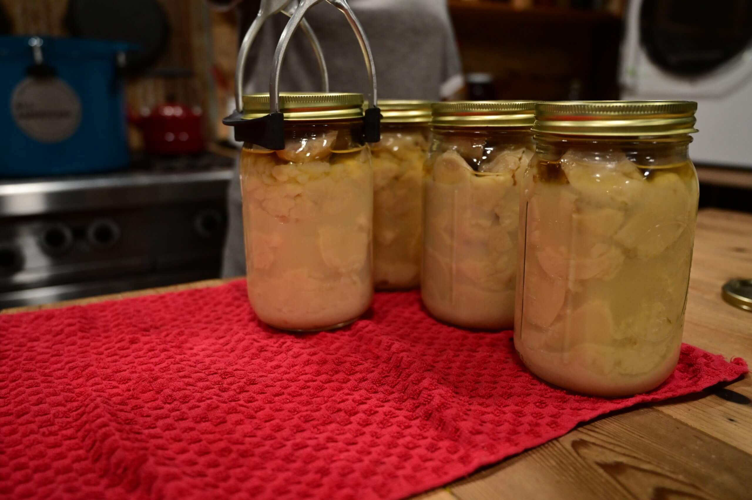 Finished jars of canned potatoes being lined up on a towel-lined kitchen counter.