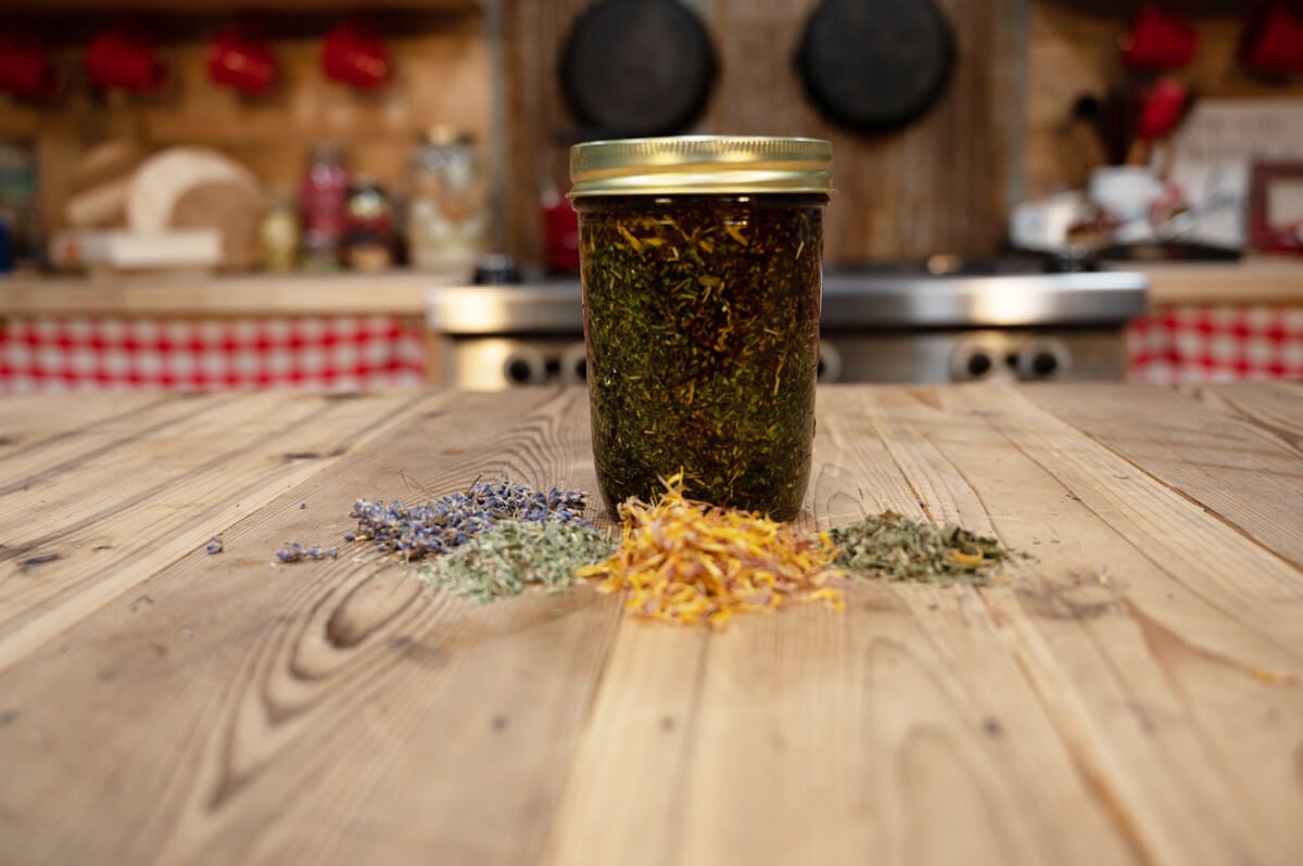 Herbal oil in a glass jar on a wooden counter.